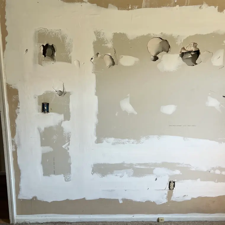 Bedroom wall with holes roughly patched over, before renovation